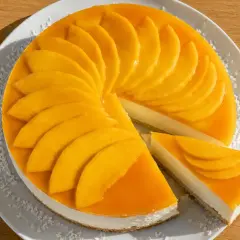 En krämig mango cheesecake med färska mangoskivor som pryder toppen. En bit är uppskuren och visar den läckra fyllningen.