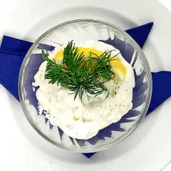 Krämig dillmajonnäs i en skål, garnerad med dill och citron. Serveras på en vit tallrik med en blå servett.