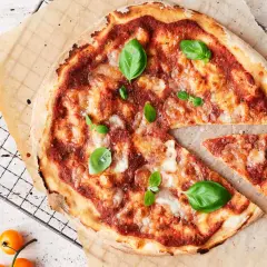 En nybakad pizza med tomatsås och ost, garnerad med färsk basilika. En bit är bortskuren. Undrar du hur många kalorier i en pizza?