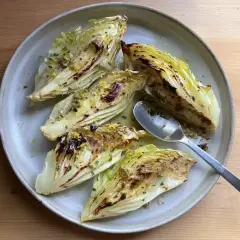 Grilla spetskål med citron och örter, serverad på en ljusgrå tallrik. En sked ligger bredvid.