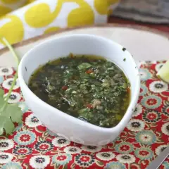 En skål med grön chimichurri, en syrlig limeklyfta och en sked på ett färgglatt tyg.