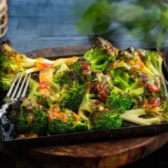 Ugnsrostad broccoli med en smakrik dressing, serverad på en plåt. Perfekt som tillbehör eller lättare måltid.