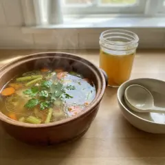 Varm kycklingsoppa med morötter och selleri i en terrakottaskål, perfekt för ett enkelt kycklingsoppa recept. En burk buljong och skålar står bredvid.