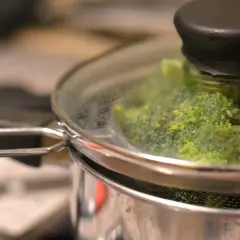 Grön broccoli ångas i en kastrull med glaslock. Snart redo att serveras!