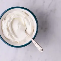 En skål med krämig gräddfil, perfekt för att lägga till smak utan för många gräddfil kcal. En silverfärgad sked vilar i skålen.