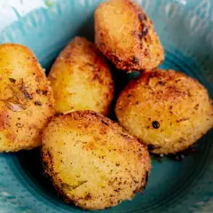 Fem gyllene, rostad potatis i ugn, kryddade med örter och peppar, serveras i en vacker turkos skål.