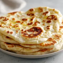 En hög med nybakade, gyllene naanbröd, perfekt för ditt nästa naan recept. Smält smör glänser på de fluffiga bröden.