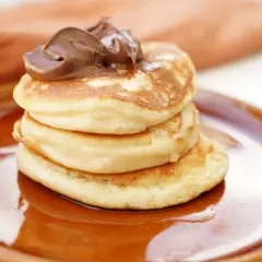 En stapel fluffiga amerikanska pannkakor toppas med chokladkräm på en brun tallrik.