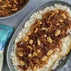 En tallrik med fluffigt basmatiris toppat med en blandning av stekt vermicelli, russin och mandlar. En påse Zeina's Quick n' Easy Basmati syns bredvid.