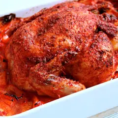 Helstekt tandoori kyckling med rostade tomater och paprika i en vit ugnsform. Kryddig och saftig.