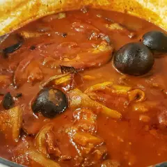 Khoresh Bademjan, a Persian eggplant stew, simmering in a pot with whole dried limes and chunks of eggplant.