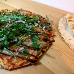 En läcker vegetarisk pizza med ruccola och rödlök, perfekt för dig som söker vegetariska recept. Bredvid ligger nybakade pitabröd.