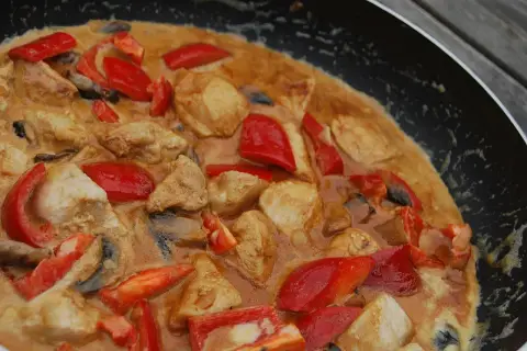 En krämig asiatisk kycklingrätt med paprika och champinjoner i en panna.