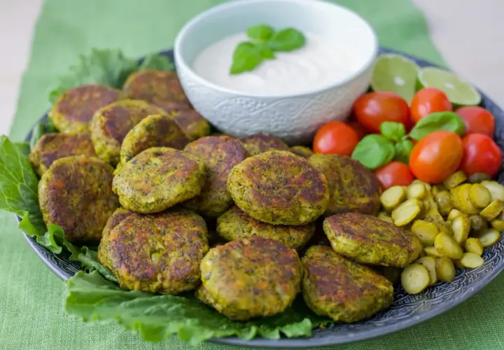 En tallrik med gyllene vegetariska biffar, serverade med en krämig dipp, körsbärstomater, gurkskivor och limeklyftor.