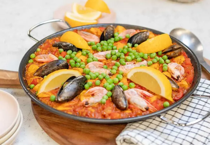 En stor paella med räkor, musslor, gröna ärtor och citronklyftor. Perfekt för ett somrigt paella recept.
