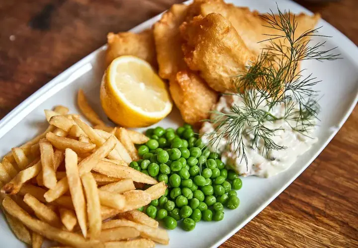 En tallrik med fish and chips, ärtor, citronklyfta och remouladsås.