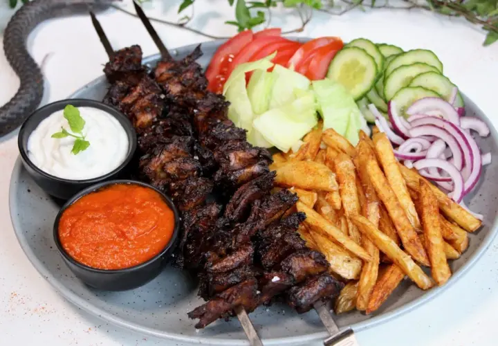 En tallrik med vegetarisk kebab på spett, serverad med pommes frites, sallad, tomat, gurka, rödlök, vit sås och en röd sås.