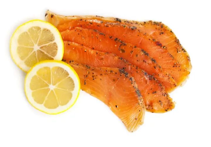 Skivor av gravad regnbåge med peppar och två citronskivor på vit bakgrund.