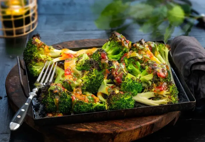 Ugnsrostad broccoli med en smakrik dressing, serverad på en plåt. Perfekt som tillbehör eller lättare måltid.