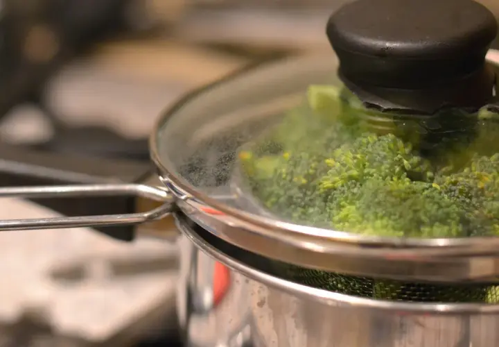 Grön broccoli ångas i en kastrull med glaslock. Snart redo att serveras!