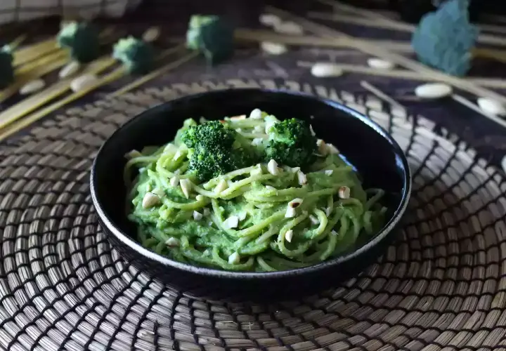 En skål med krämig broccoli pasta, toppad med broccolibuketter och hackade nötter. En härlig och grön måltid.