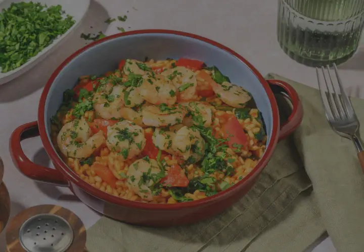 En härlig paella valenciana med saftiga räkor, paprika och ris, toppad med färsk persilja.