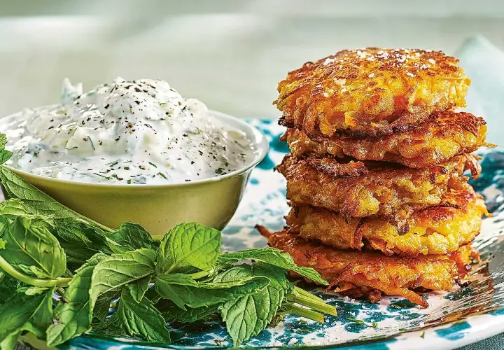 En stapel gyllene halloumi morotsbiffar serveras med en krämig yoghurtsås och färsk mynta.