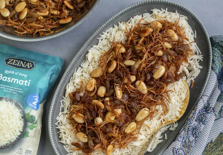 En tallrik med fluffigt basmatiris toppat med en blandning av stekt vermicelli, russin och mandlar. En påse Zeina's Quick n' Easy Basmati syns bredvid.