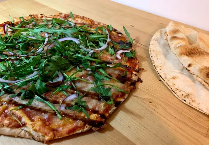 En läcker vegetarisk pizza med ruccola och rödlök, perfekt för dig som söker vegetariska recept. Bredvid ligger nybakade pitabröd.