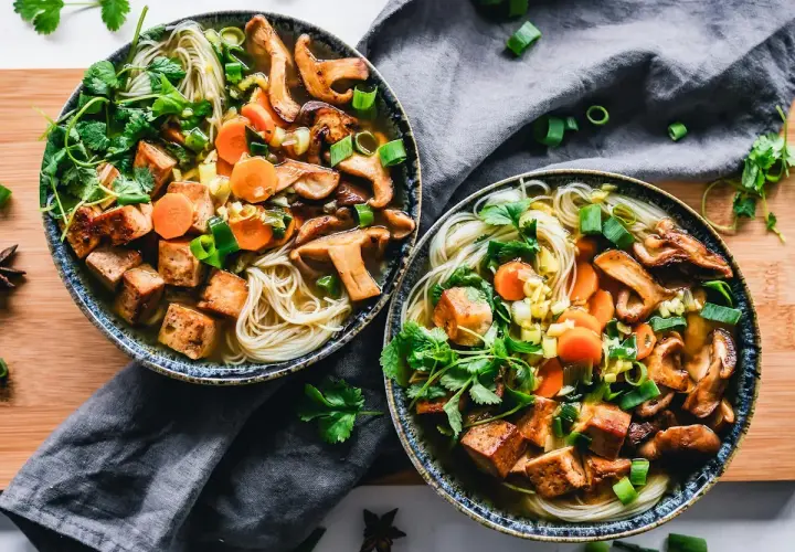 Två skålar med nudlar, svamp, morötter och krispiga tofu-bitar. Ett perfekt tofu recept för en värmande måltid.