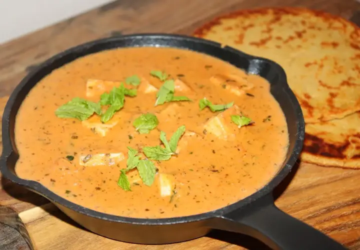 En krämig paneer-rätt i en gjutjärnspanna, garnerad med mynta. Bredvid ligger två gyllene, tunna bröd. Ett perfekt paneer recept!