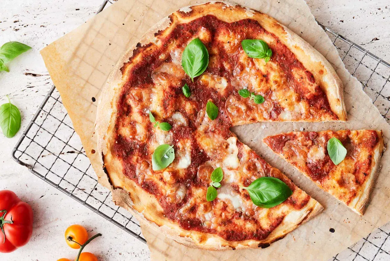 En nybakad pizza med tomatsås och ost, garnerad med färsk basilika. En bit är bortskuren. Undrar du hur många kalorier i en pizza?