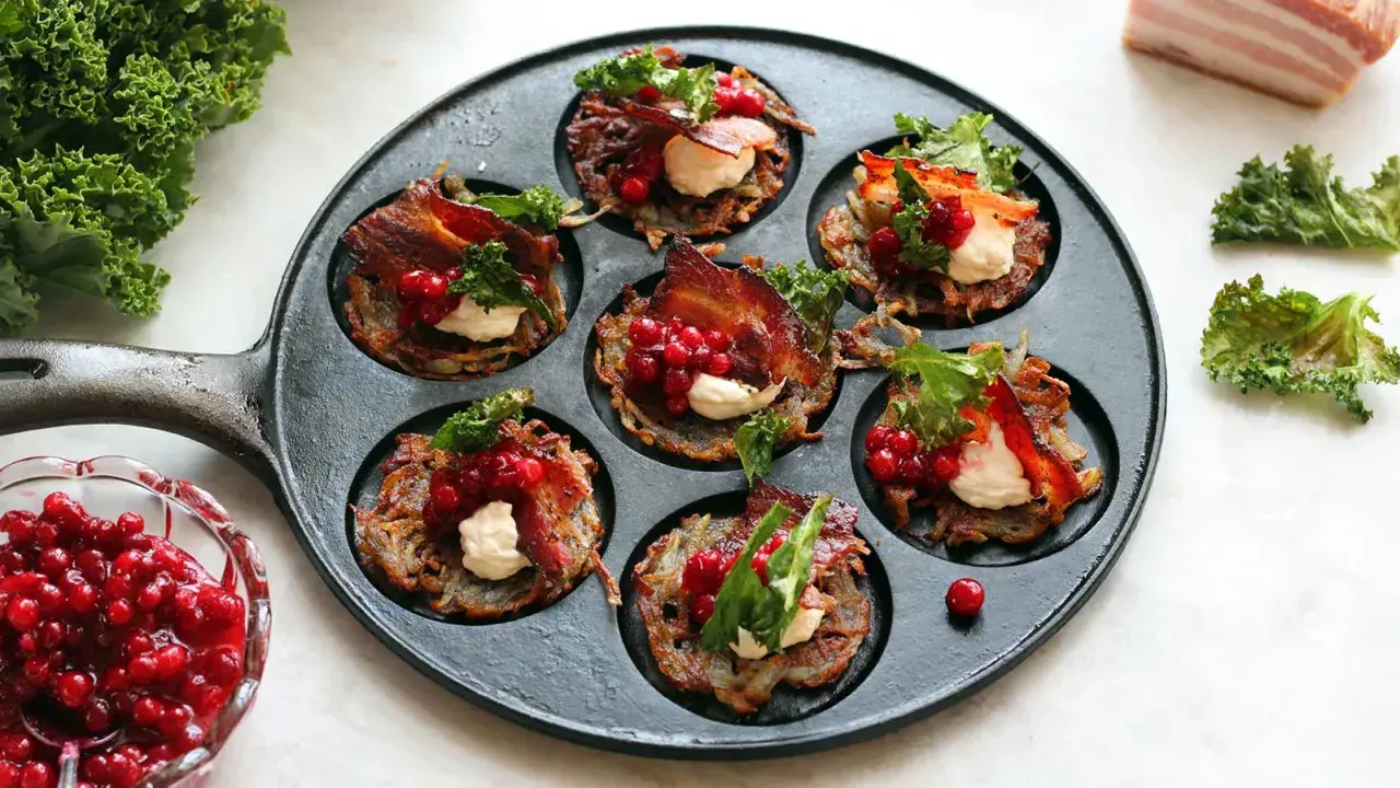 Små, krispiga rårakor med bacon, gräddfil och rårörda lingon i en gjutjärnspanna. Serveras med färska lingon och grönkål.