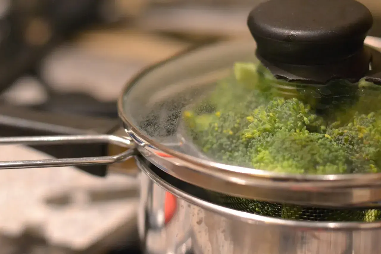 Grön broccoli ångas i en kastrull med glaslock. Snart redo att serveras!