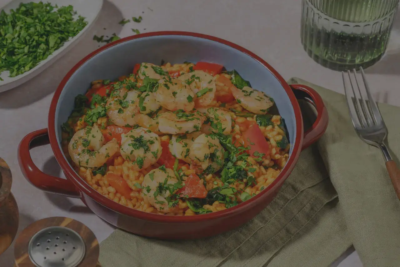 En härlig paella valenciana med saftiga räkor, paprika och ris, toppad med färsk persilja.