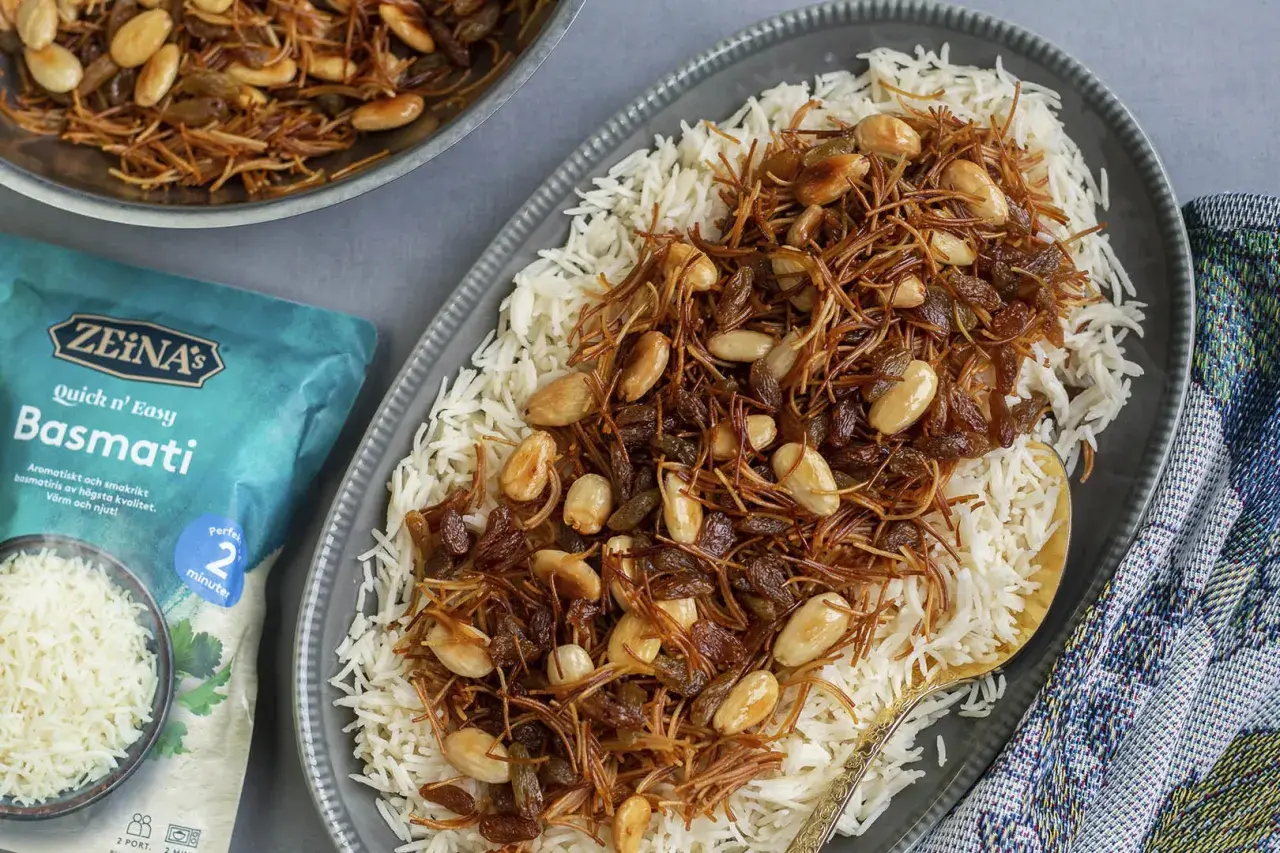 En tallrik med fluffigt basmatiris toppat med en blandning av stekt vermicelli, russin och mandlar. En påse Zeina's Quick n' Easy Basmati syns bredvid.