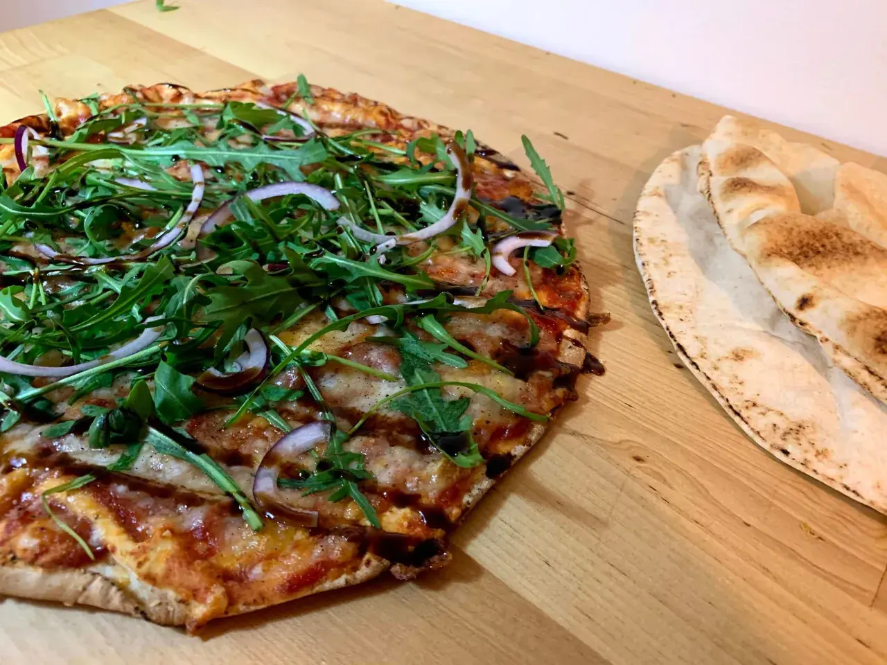 En läcker vegetarisk pizza med ruccola och rödlök, perfekt för dig som söker vegetariska recept. Bredvid ligger nybakade pitabröd.