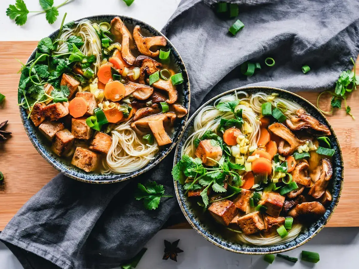 Två skålar med nudlar, svamp, morötter och krispiga tofu-bitar. Ett perfekt tofu recept för en värmande måltid.