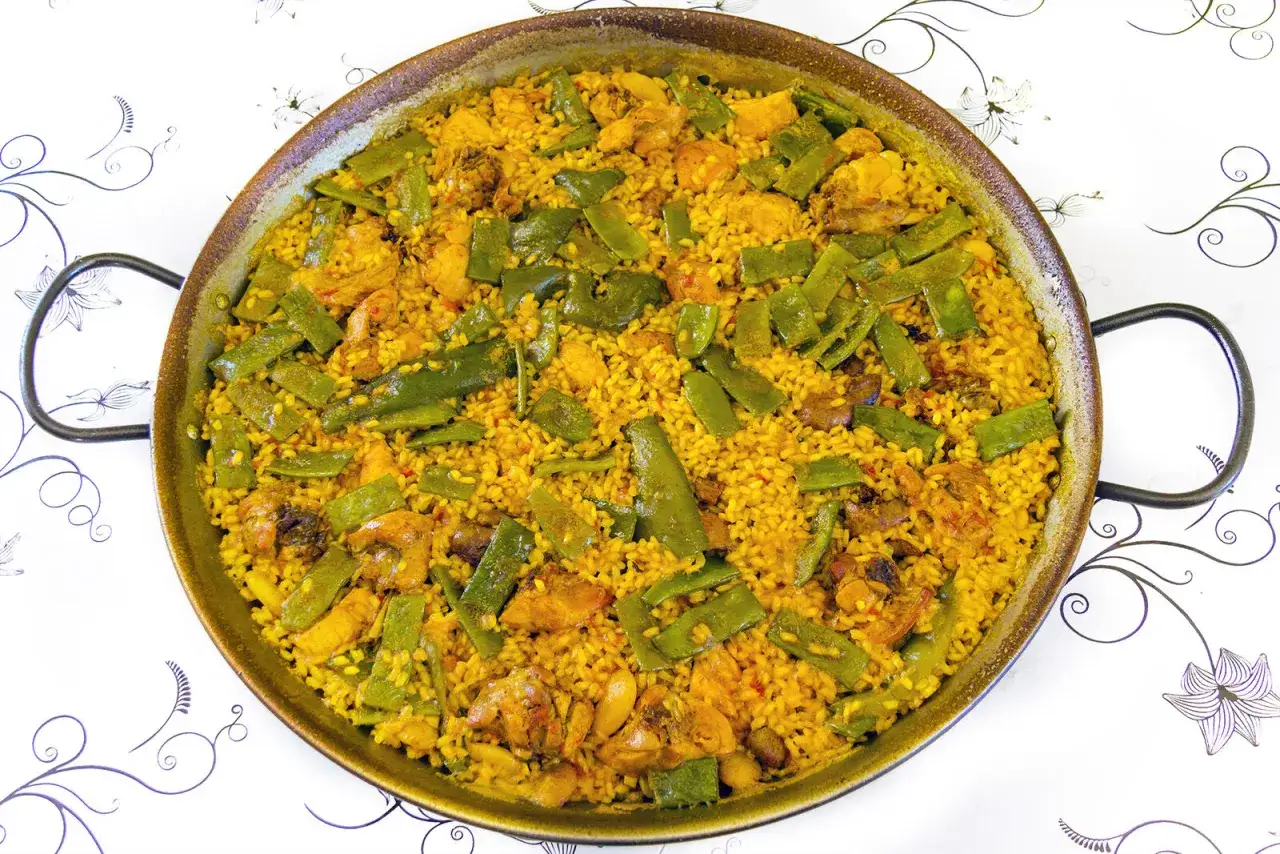 En stor paella valenciana med ris, kyckling och gröna bönor i en panna.