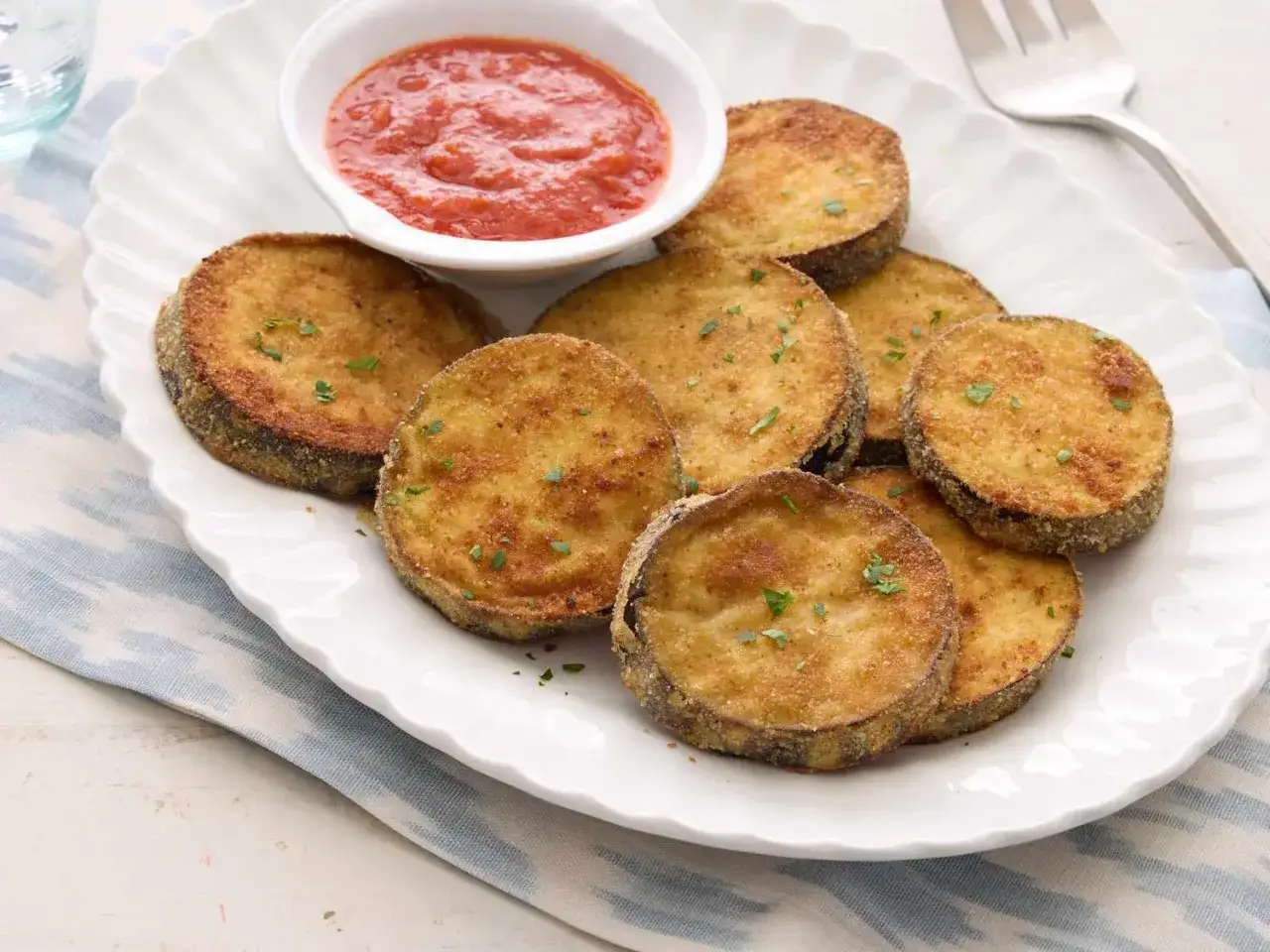 Krispigt panerad och gyllene stekt aubergine serveras med en skål tomatsås. Perfekt som tillbehör eller förrätt.