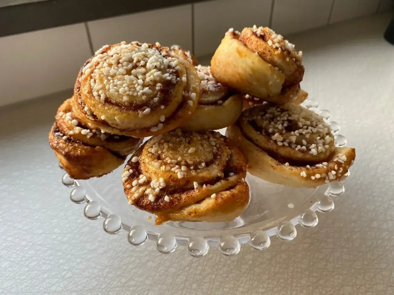 En hög med kanelbullar på ett glasfat, redo för en mysig fika.