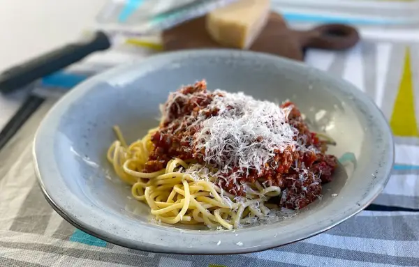 En tallrik spaghetti med en mustig, gammaldags köttfärssås och rikligt med riven parmesanost.